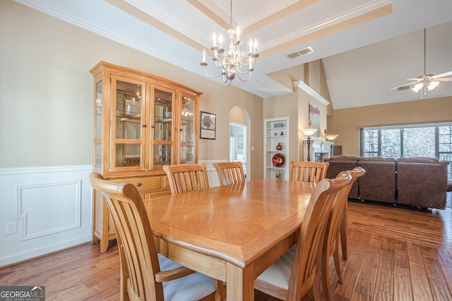 dining space with arched walkways, a chandelier, built in features, light wood-type flooring, and a wainscoted wall