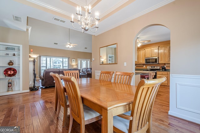 dining space featuring a ceiling fan, light wood-style flooring, crown molding, arched walkways, and a chandelier