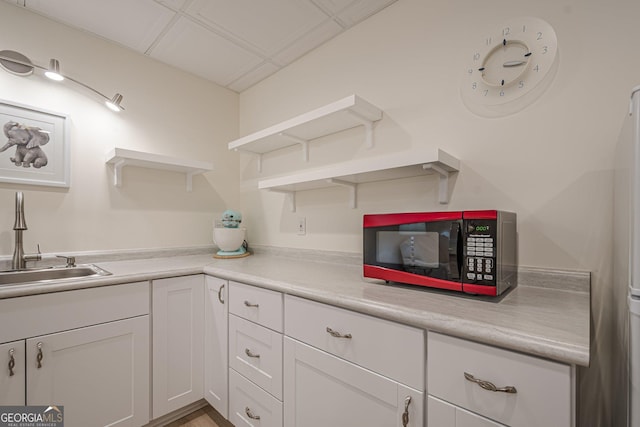 kitchen with open shelves, white cabinets, light countertops, and a sink