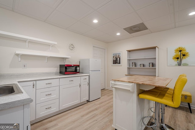 kitchen featuring open shelves, light wood finished floors, freestanding refrigerator, a kitchen breakfast bar, and recessed lighting