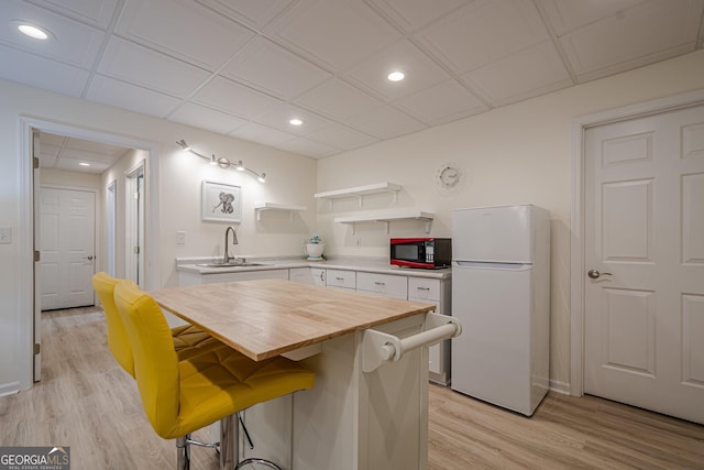 kitchen featuring freestanding refrigerator, black microwave, open shelves, light wood finished floors, and recessed lighting