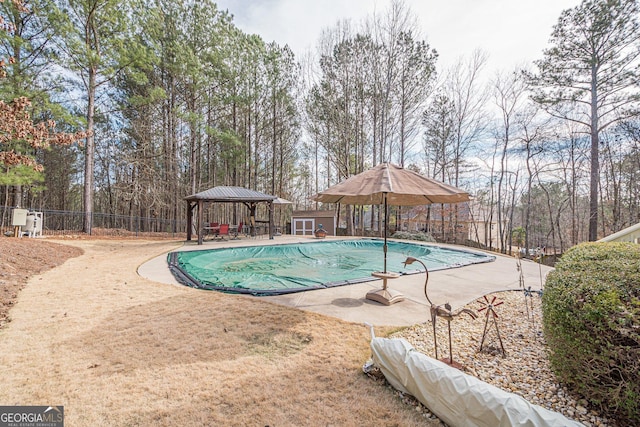 view of pool with a gazebo, fence, a patio area, and view of scattered trees