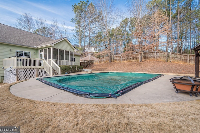 view of pool with a sunroom, a fenced backyard, an outdoor fire pit, and a patio area