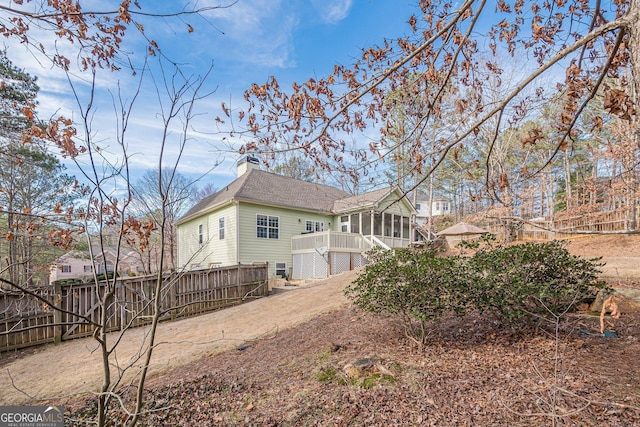 rear view of property featuring a chimney, a sunroom, a wooden deck, a fenced backyard, and a shingled roof