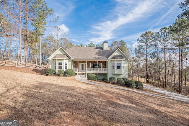 view of front facade featuring fence, roof with shingles, covered porch, a front yard, and a chimney