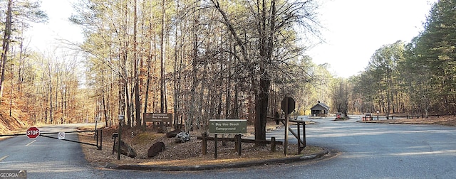 view of asphalt street featuring traffic signs, a view of trees, and curbs