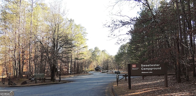 view of asphalt road featuring a view of trees and curbs