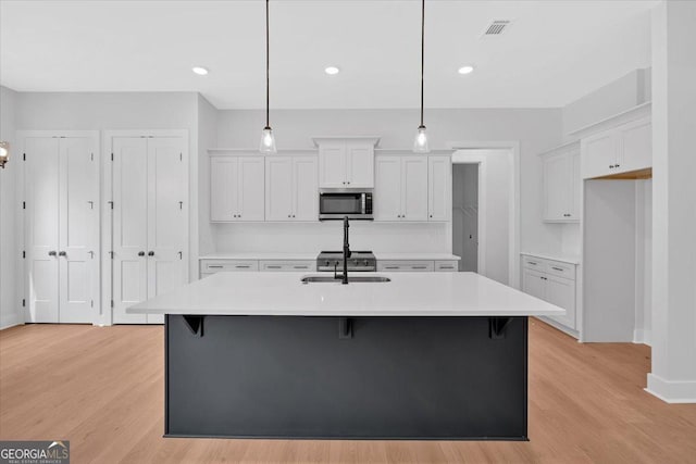 kitchen featuring stainless steel microwave, white cabinetry, light wood finished floors, light countertops, and recessed lighting