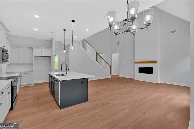 kitchen with appliances with stainless steel finishes, a sink, white cabinets, hanging light fixtures, and light wood finished floors