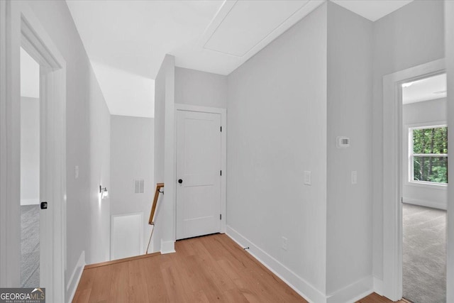 corridor with an upstairs landing, light wood-style floors, baseboards, and attic access