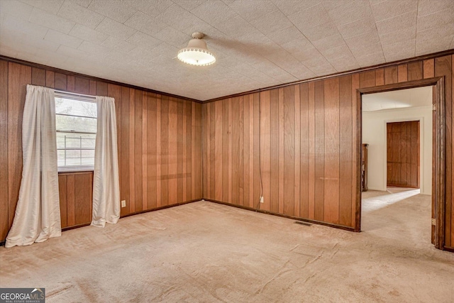 empty room featuring wooden walls, ornamental molding, and light colored carpet