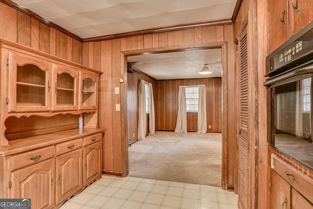 hall with ornamental molding, light carpet, wood walls, and light floors