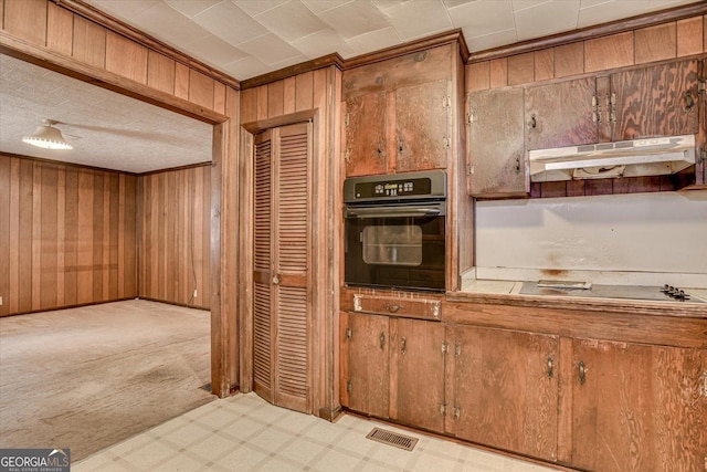 kitchen featuring tile countertops, light floors, wooden walls, under cabinet range hood, and black appliances