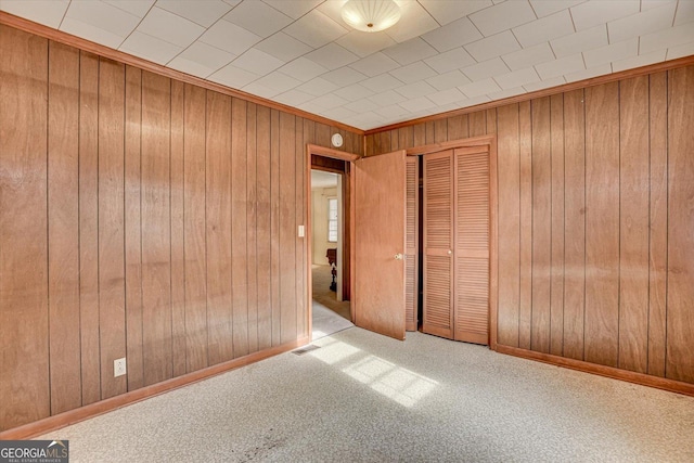 spare room with wood walls, baseboards, visible vents, and light colored carpet