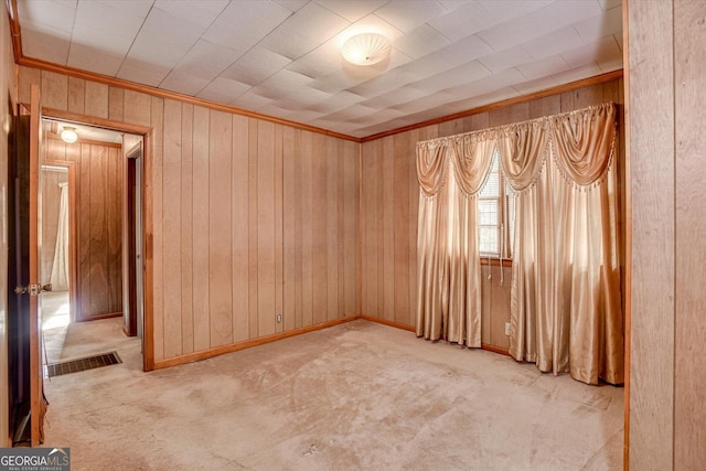 unfurnished room with light carpet, wood walls, visible vents, and crown molding