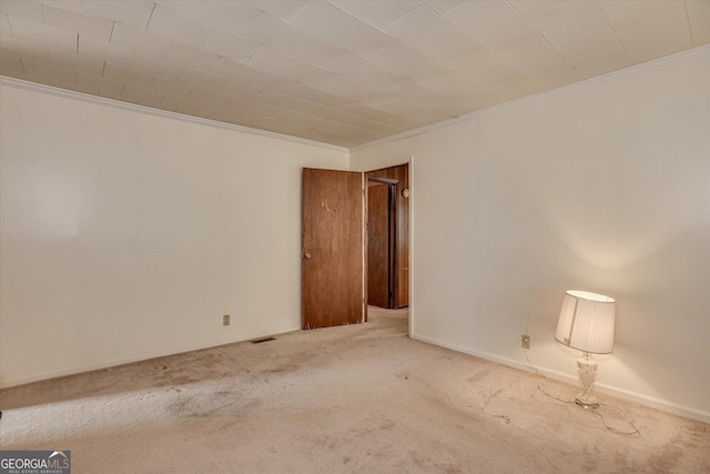 empty room featuring carpet floors, visible vents, baseboards, and crown molding