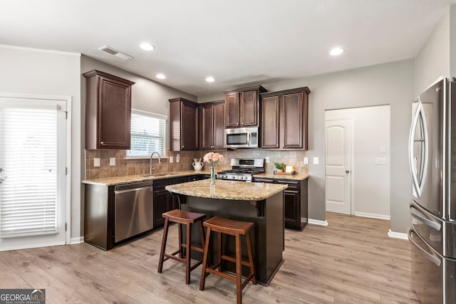 kitchen with a center island, visible vents, appliances with stainless steel finishes, a sink, and dark brown cabinetry