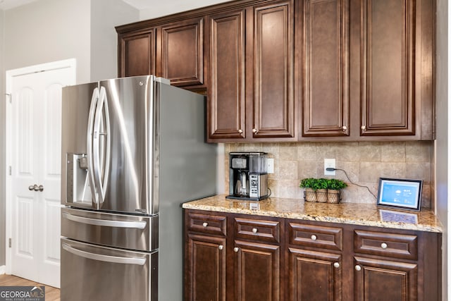 kitchen with dark brown cabinetry, stainless steel fridge, light stone counters, and tasteful backsplash