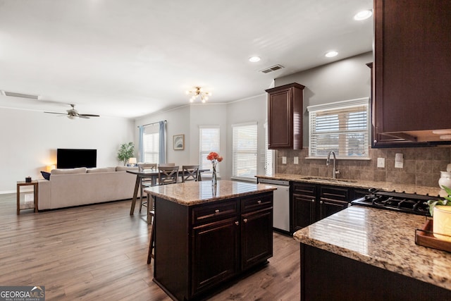 kitchen with light stone counters, a center island, visible vents, a sink, and dishwasher