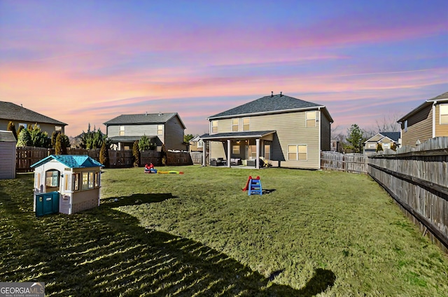 back of house at dusk with a lawn, a playground, and a fenced backyard