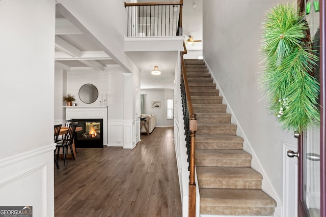 entryway featuring beam ceiling, a decorative wall, dark wood-type flooring, a glass covered fireplace, and coffered ceiling