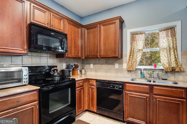 kitchen with tasteful backsplash, brown cabinets, light countertops, black appliances, and a sink