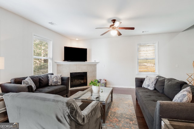 living room with a fireplace, visible vents, dark wood-type flooring, ceiling fan, and baseboards