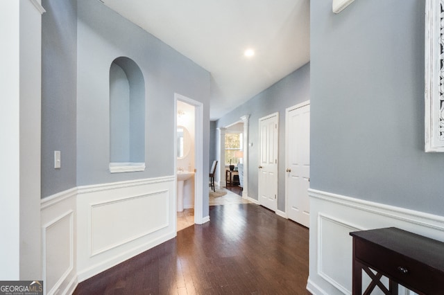 corridor with a wainscoted wall, dark wood-type flooring, and a decorative wall