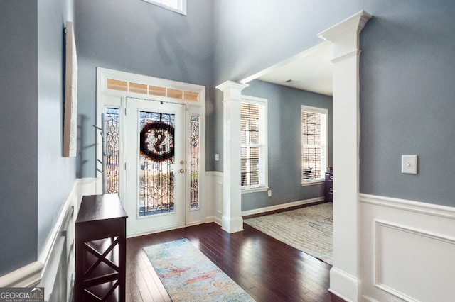 entrance foyer featuring a wainscoted wall, dark wood-style flooring, and ornate columns