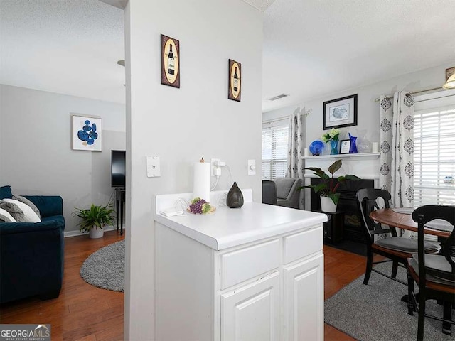 kitchen featuring visible vents, open floor plan, wood finished floors, light countertops, and white cabinetry