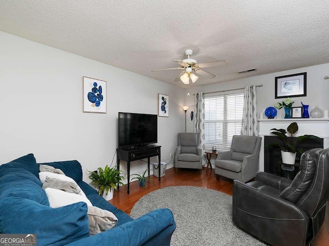 living room with dark wood-type flooring, visible vents, ceiling fan, and a textured ceiling