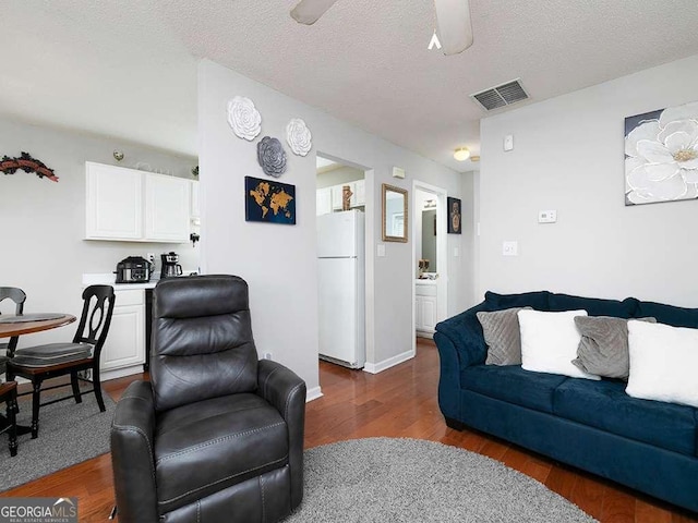 living area with dark wood finished floors, visible vents, a ceiling fan, a textured ceiling, and baseboards