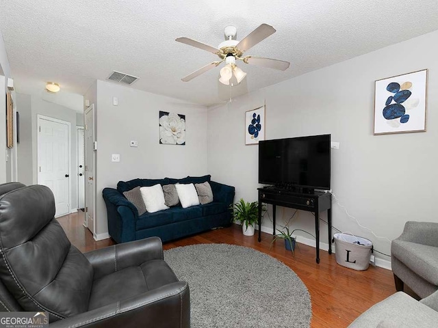living area featuring a textured ceiling, wood finished floors, visible vents, and a ceiling fan