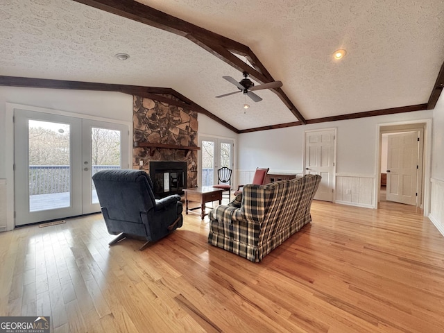 living room with a wainscoted wall, french doors, vaulted ceiling with beams, and light wood-type flooring