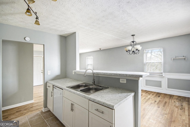 kitchen featuring pendant lighting, white cabinets, a sink, light stone countertops, and dishwasher