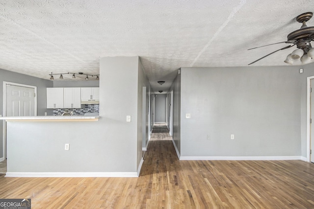 unfurnished living room with a textured ceiling, wood finished floors, a ceiling fan, and baseboards