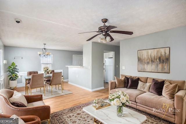 living area with ceiling fan with notable chandelier, a textured ceiling, light wood-style flooring, and baseboards