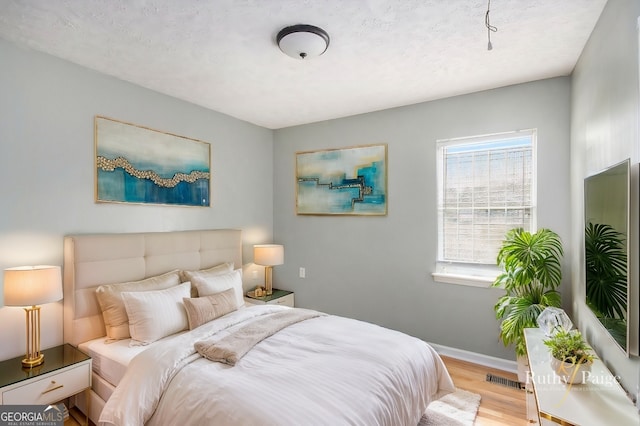 bedroom with visible vents, light wood-style flooring, baseboards, and a textured ceiling