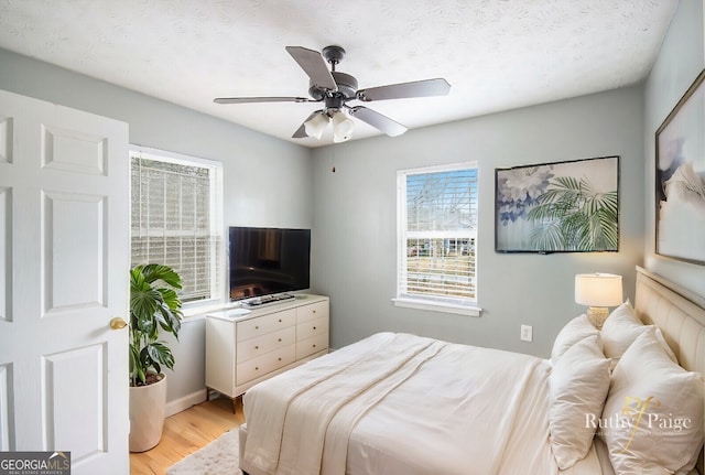 bedroom featuring light wood finished floors, ceiling fan, and a textured ceiling