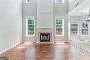 unfurnished living room featuring wood finished floors, a fireplace with flush hearth, a towering ceiling, and a healthy amount of sunlight