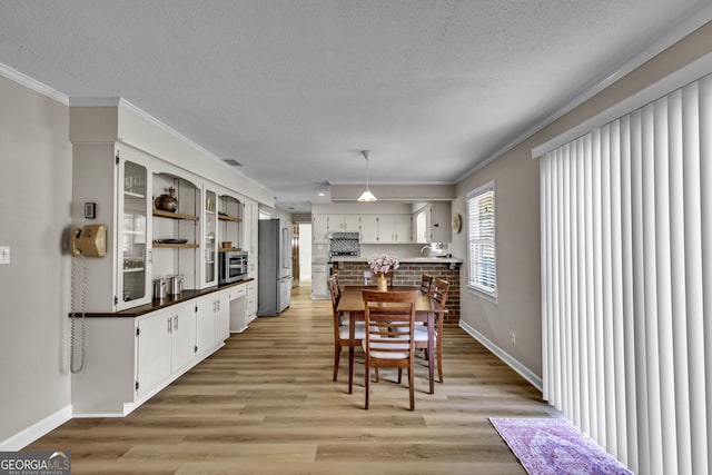 dining room featuring a textured ceiling, light wood-type flooring, baseboards, and crown molding