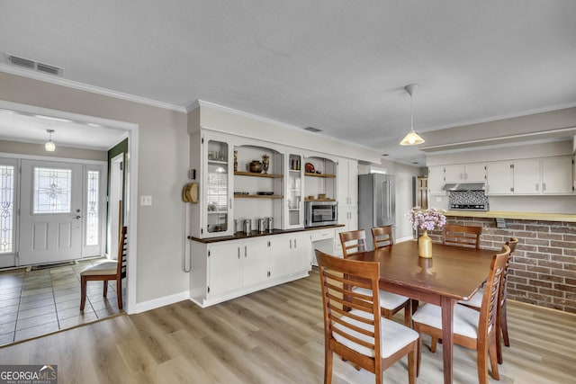 dining room with light wood-type flooring, visible vents, and ornamental molding