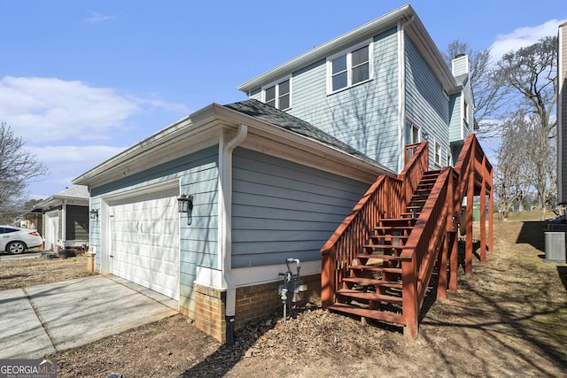 view of side of property with a garage, a shingled roof, stairs, concrete driveway, and a chimney