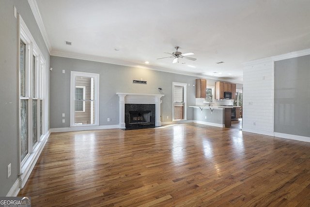 unfurnished living room with ceiling fan, a fireplace, ornamental molding, and wood finished floors