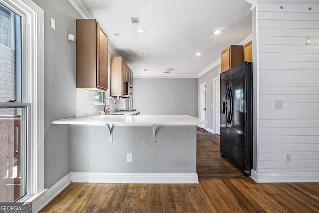 kitchen with dark wood finished floors, light countertops, black refrigerator with ice dispenser, brown cabinetry, and a peninsula