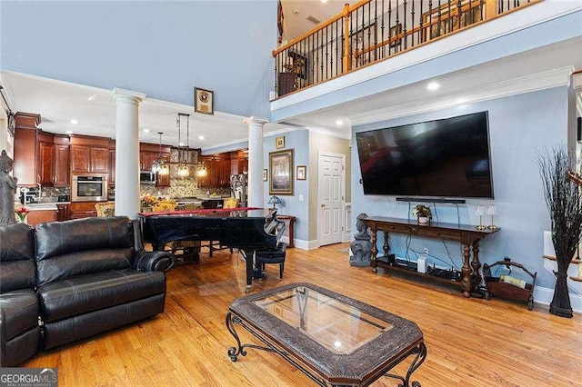 living room with crown molding, decorative columns, light wood-style flooring, a high ceiling, and baseboards