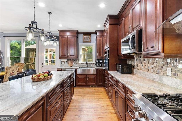 kitchen with light stone counters, hanging light fixtures, stainless steel appliances, crown molding, and a sink