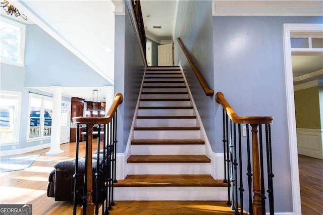 staircase with ornamental molding, wood finished floors, and decorative columns