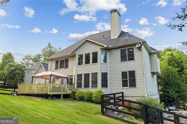 rear view of property featuring a chimney, a lawn, a gazebo, fence, and a deck