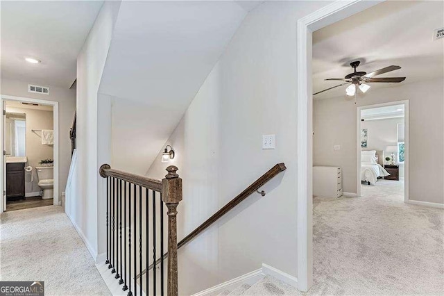 hallway featuring light carpet, visible vents, and an upstairs landing